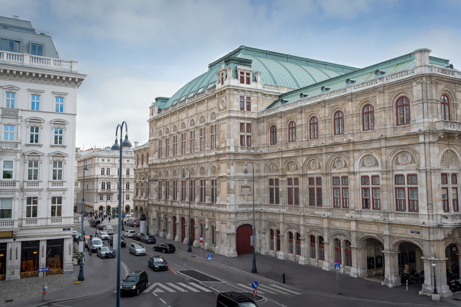 Wiener Staatsoper at dusk, lit warmly against a deepening blue sky, with passers-by on the Ringstrasse.